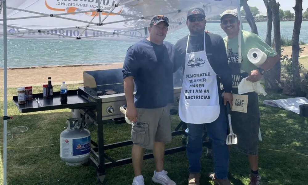 Three men standing next to a grill with an apron on.