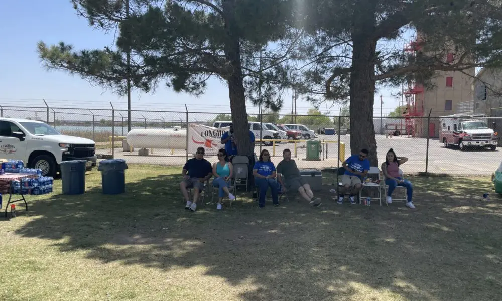 A group of people sitting in chairs under trees.