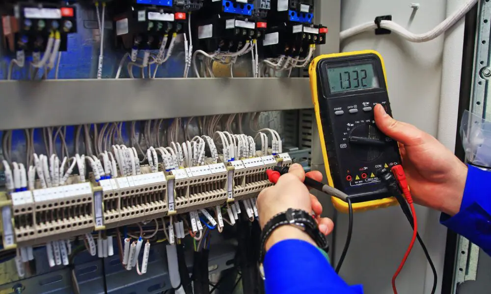 A person is holding a multimeter in front of some wires.