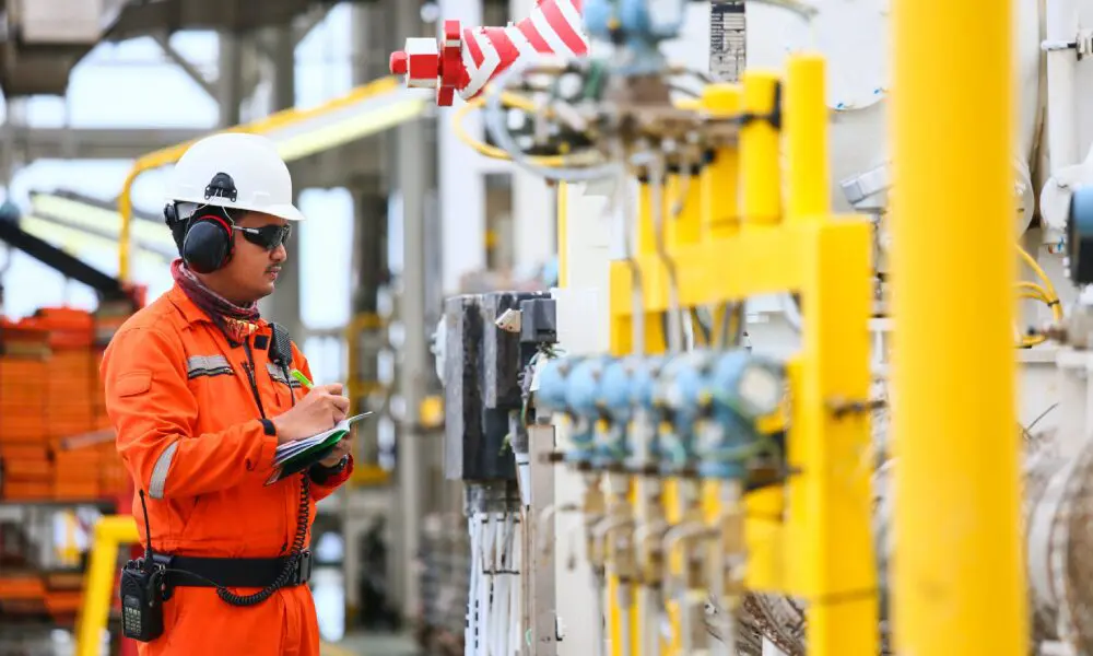 A man in an orange suit is looking at some pipes.