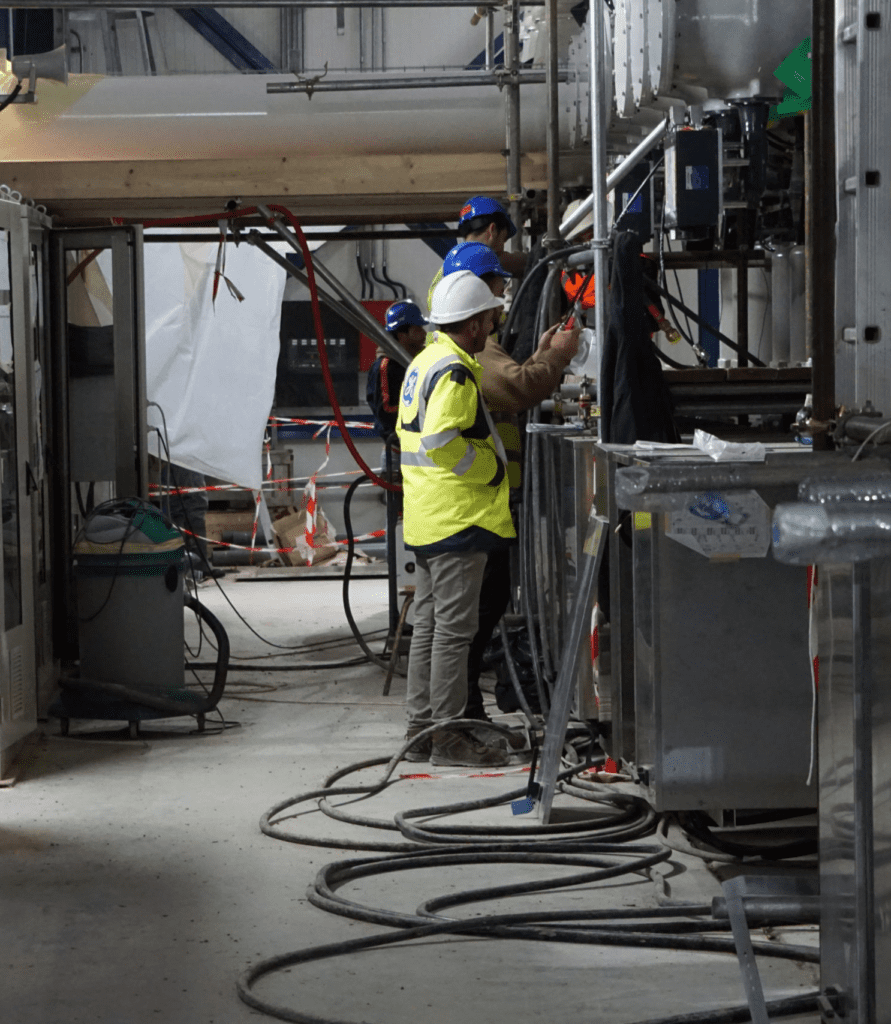 A man in yellow vest and hard hat working on machine.