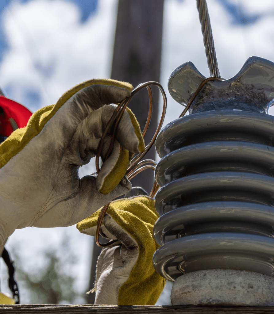 A person with gloves on holding onto an electrical wire.